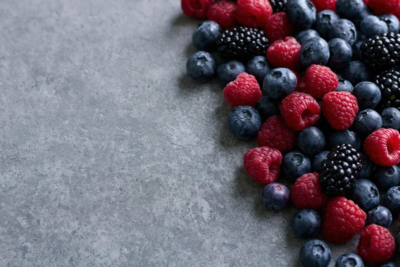 Mixed fresh berries arranged in corner on gray stone surface