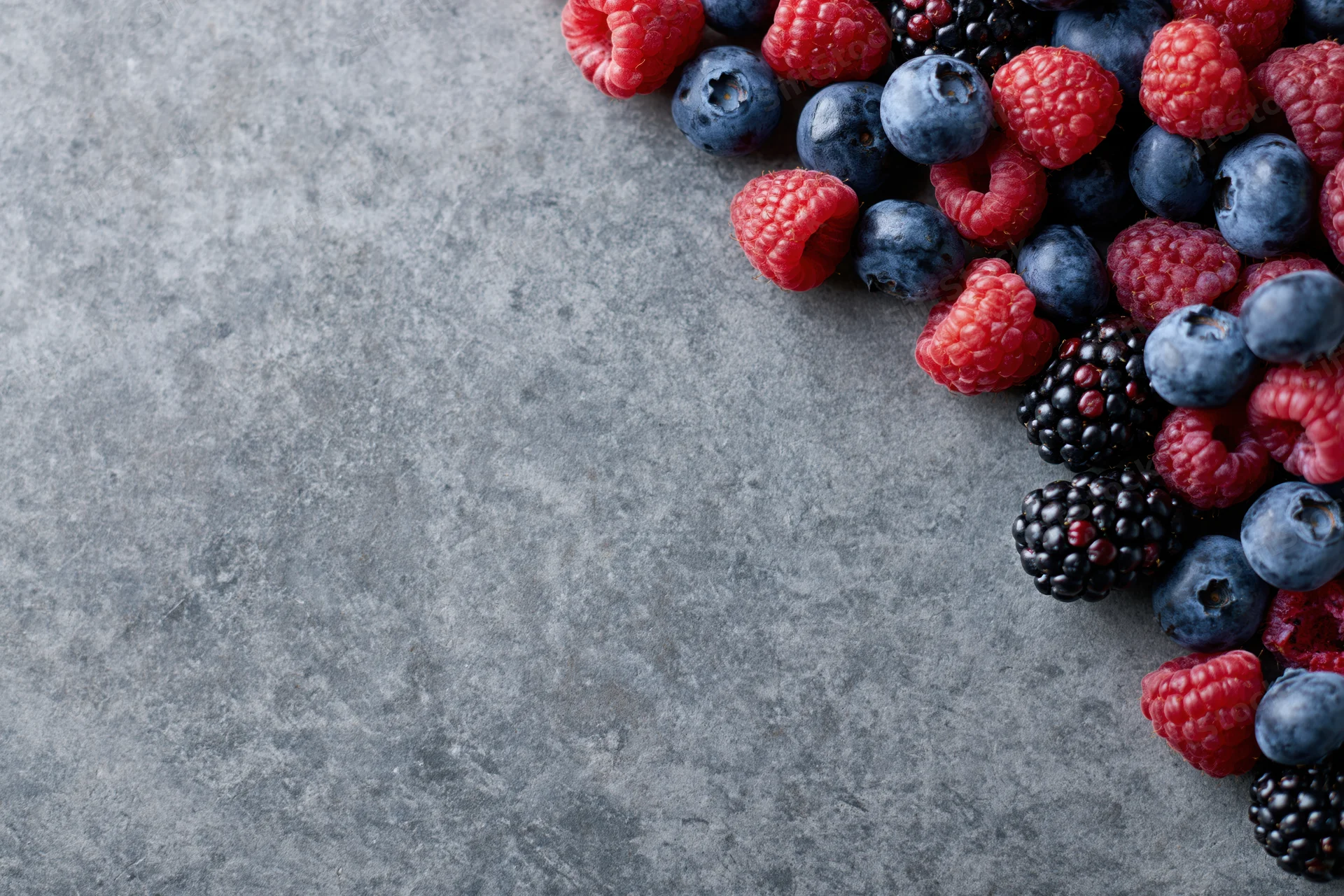 Mixed fresh berries arranged on a gray stone surface with copyspace
