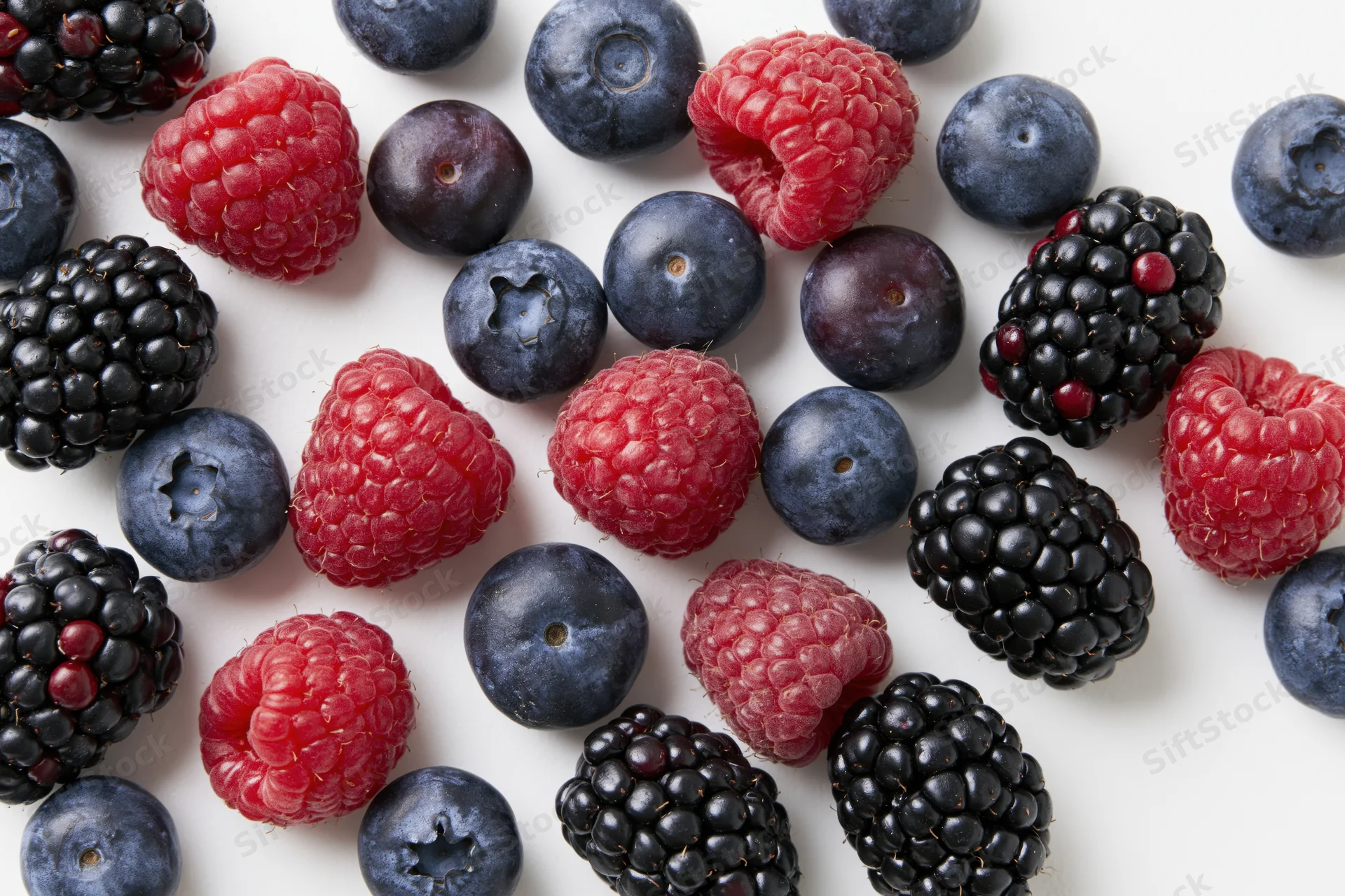 Mixed fresh blueberries raspberries and blackberries arranged on white surface