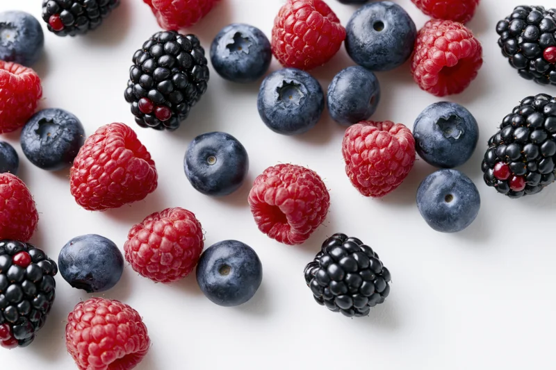 Mixed fresh berries arranged on white surface in flat lay view