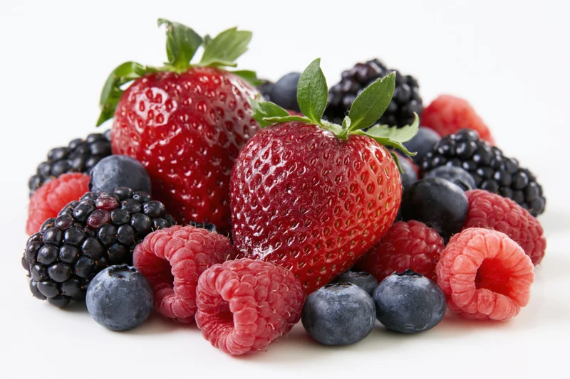 Mixed fresh berries including strawberries raspberries blueberries and blackberries arranged in a casual cluster on a white surface