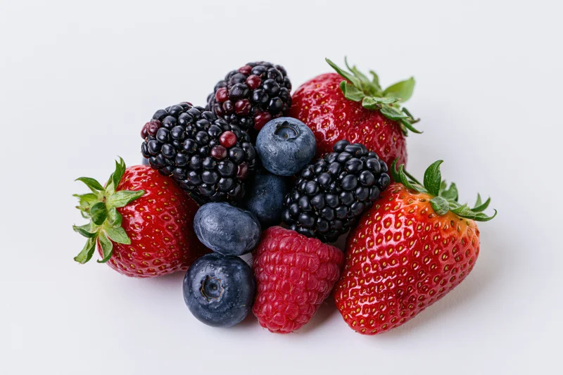Mixed fresh berries including strawberries, blackberries, blueberries and raspberries arranged in a cluster on a white surface