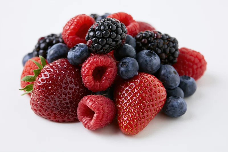 Pile of fresh strawberries blueberries raspberries and blackberries on white background