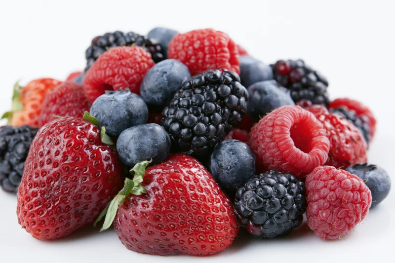 Pile of fresh strawberries blueberries raspberries and blackberries on white background