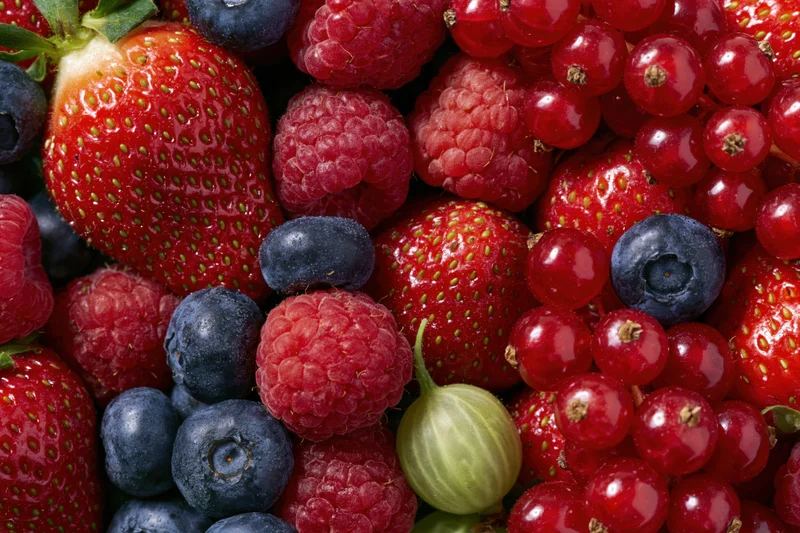 Mixed fresh berries including strawberries blueberries raspberries and redcurrants piled together in a closeup view