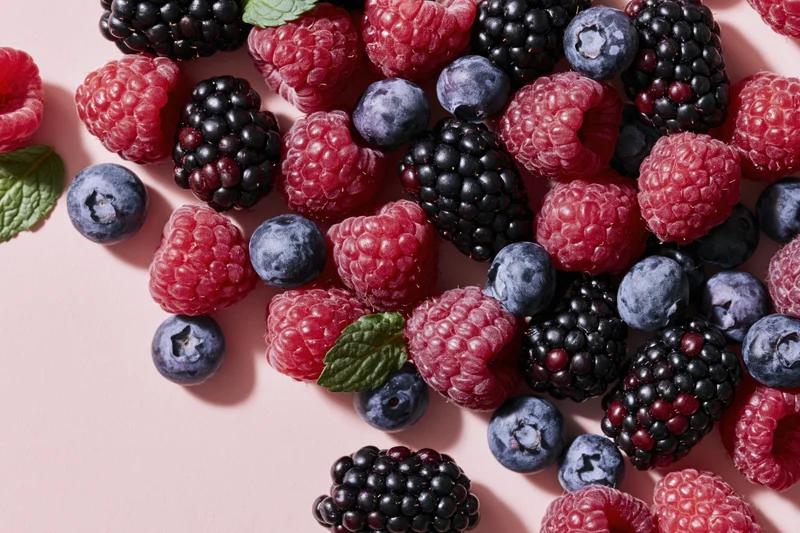 Mixed fresh berries including raspberries blackberries and blueberries arranged on a pink surface with mint leaves