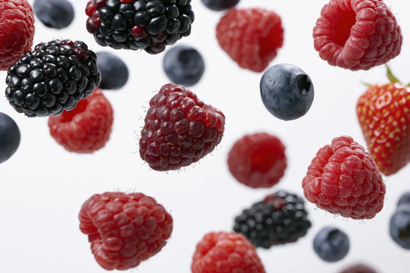 Mixed fresh berries floating against a white background