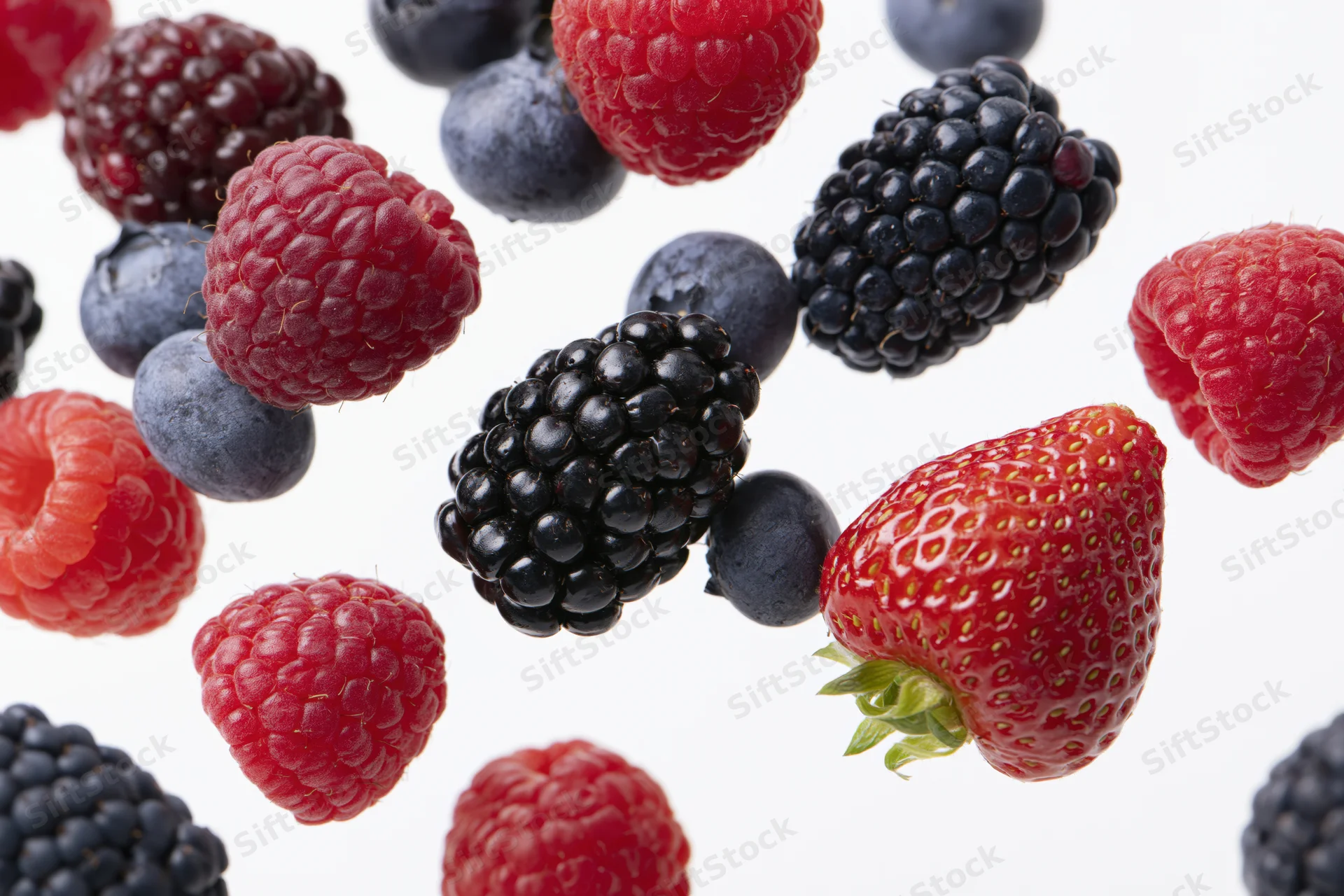 Mixed fresh berries including raspberries blackberries blueberries and strawberry arranged on white background