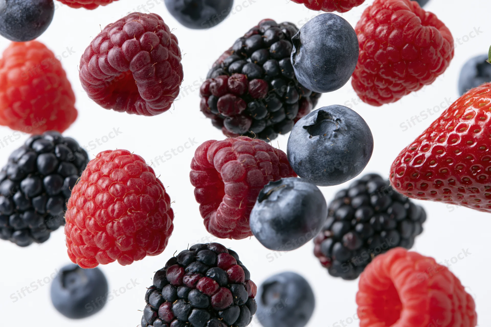 Mixed fresh berries floating against a white background