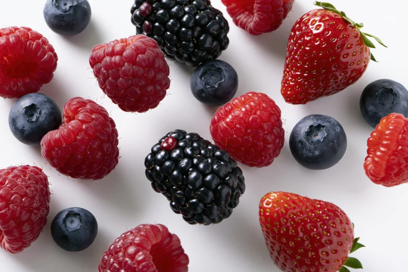 Mixed fresh berries scattered on white surface