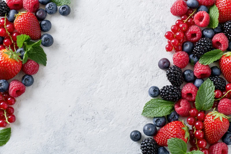 Mixed fresh berries arranged along left and right edges on textured white surface with central copyspace