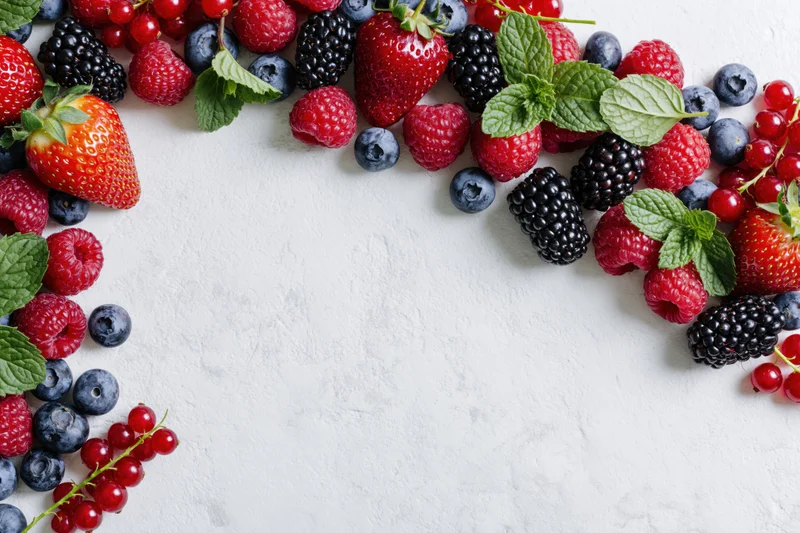 Mixed fresh berries arranged along left and right edges on white surface with copyspace in center