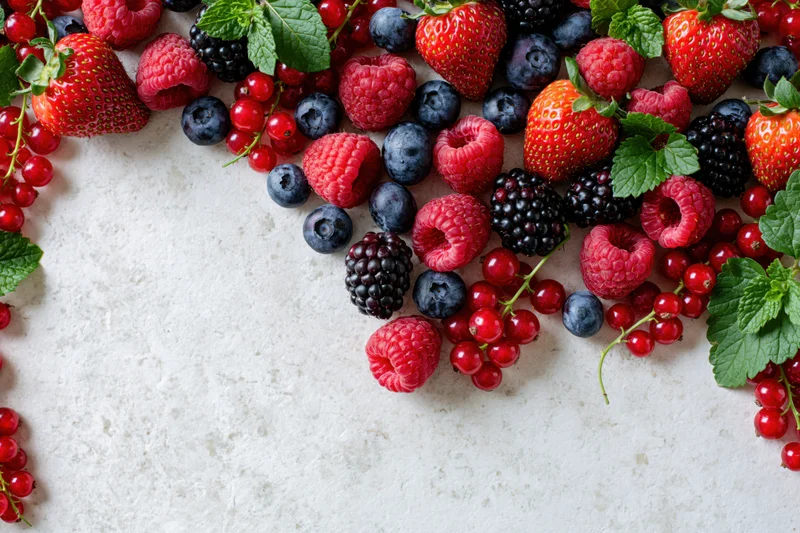 Mixed fresh berries scattered along left and right edges on white surface