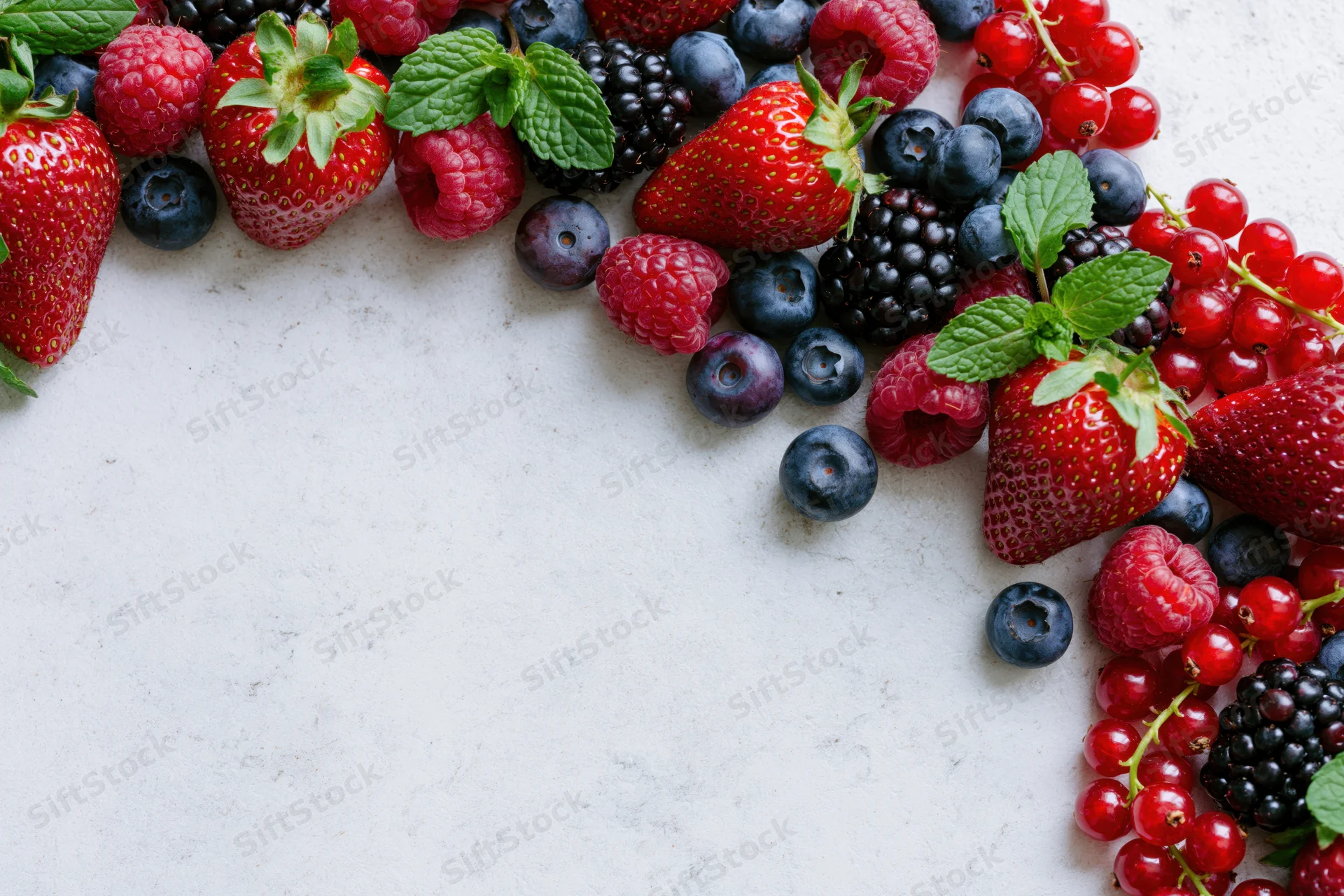 Mixed fresh berries arranged along left and right edges on white surface with copyspace