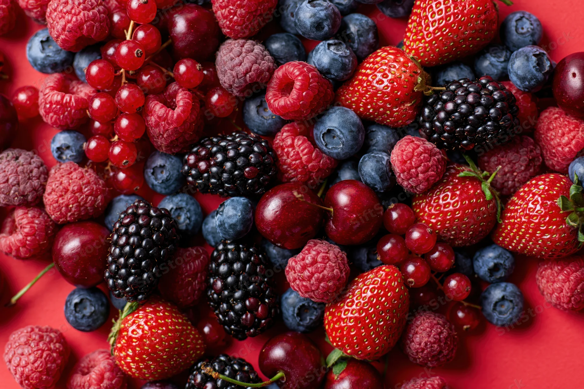 Mixed fresh berries scattered densely on a bright red surface