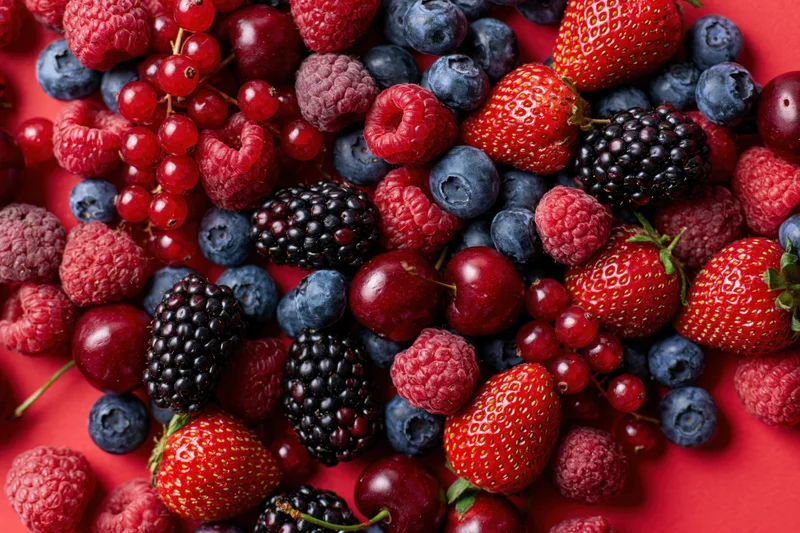 Mixed fresh berries scattered densely on a bright red surface