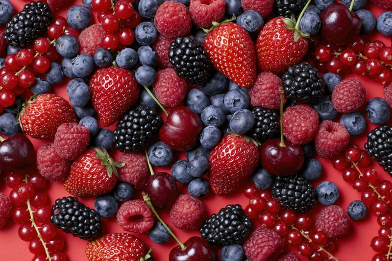 Mixed fresh berries scattered densely on a red surface