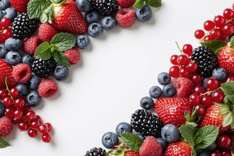 Mixed fresh berries arranged in two clusters framing a white copyspace on a flat surface