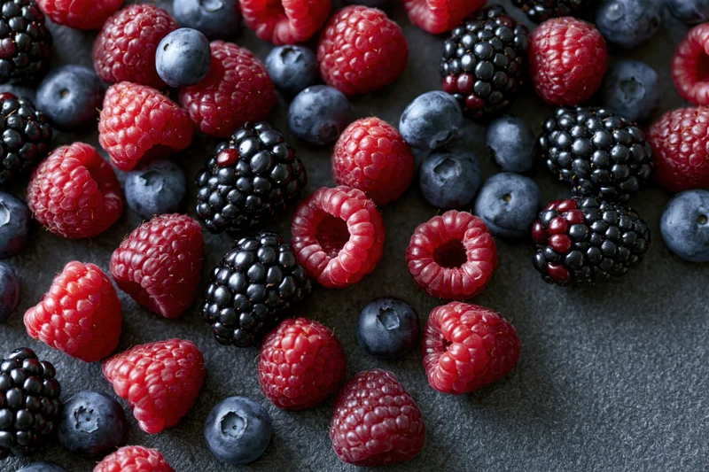 Mixed fresh berries scattered across dark matte surface in closeup top view