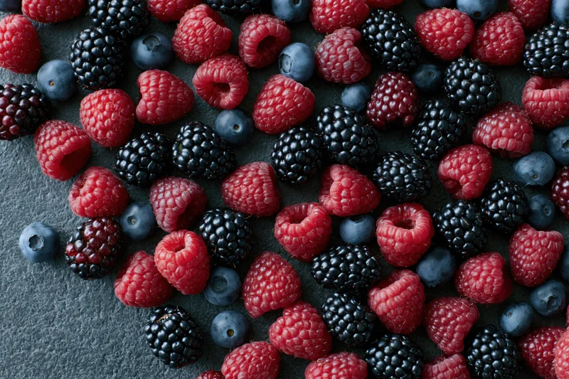 Mixed fresh berries scattered across a dark matte surface in closeup top view