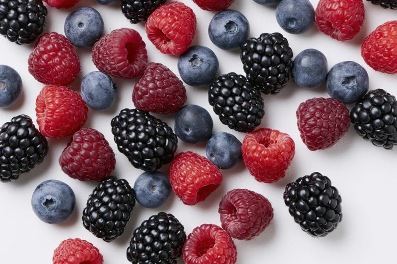 Mixed fresh berries scattered across a white background