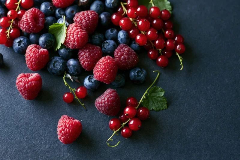 Mixed fresh berries scattered on a dark charcoal surface