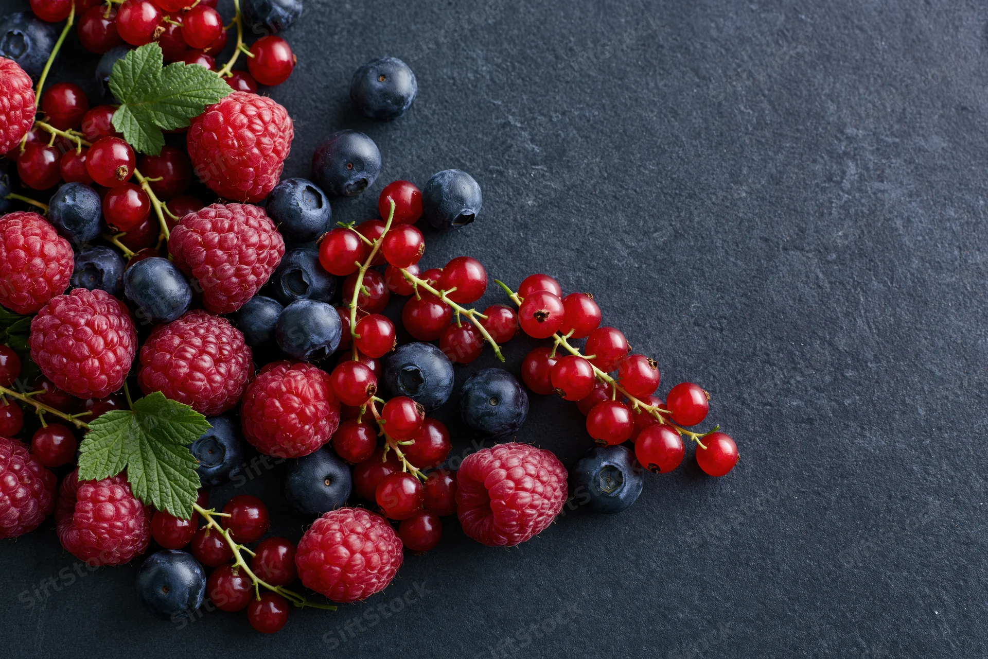 Fresh raspberries, blueberries and redcurrants scattered on a dark slate surface with copyspace