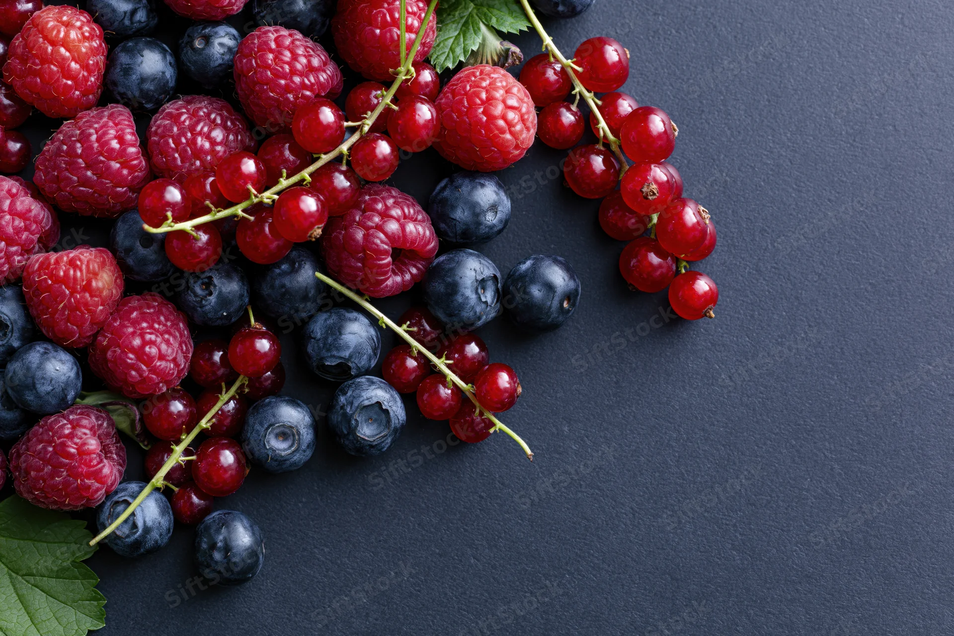 Mixed fresh berries scattered on dark charcoal surface with copyspace