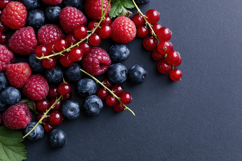 Mixed fresh berries scattered on dark charcoal surface with copyspace