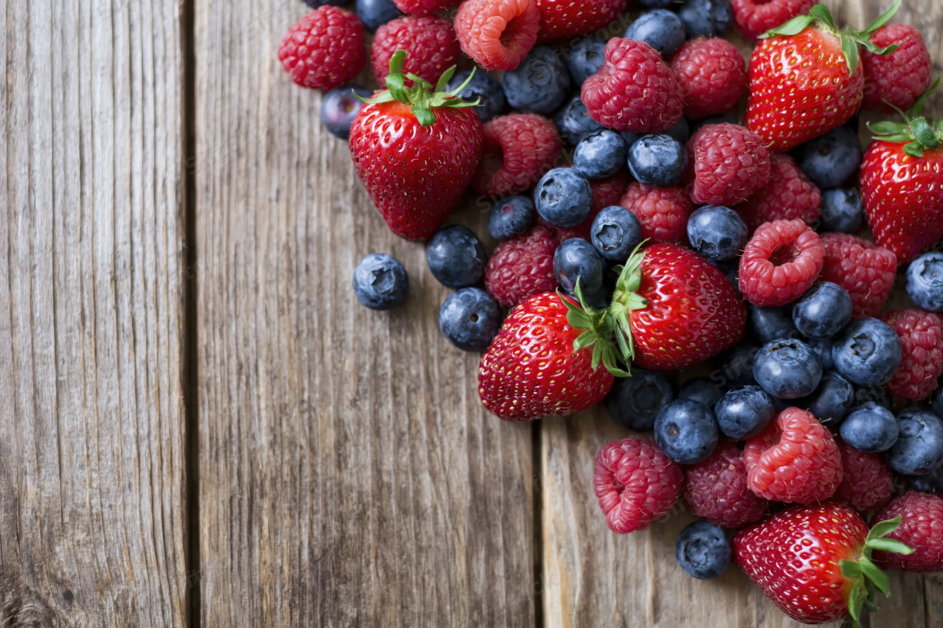 Fresh strawberries blueberries and raspberries arranged on a wooden table with copyspace on the left