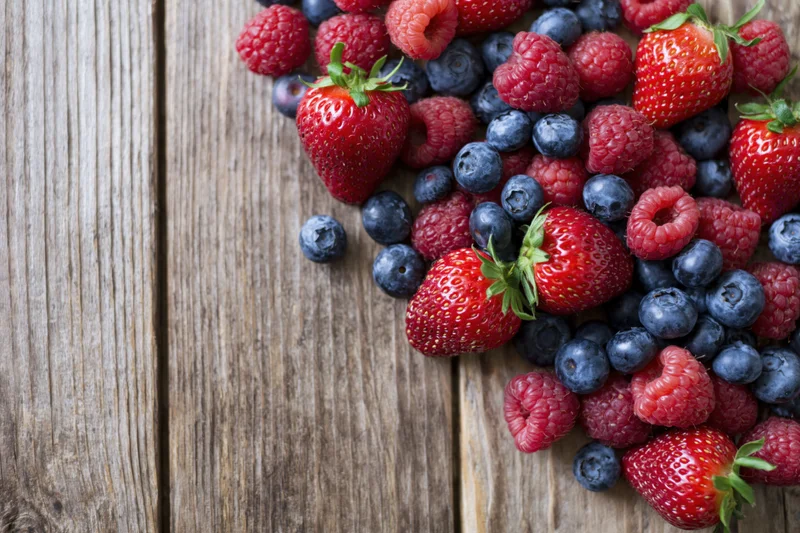 Fresh strawberries blueberries and raspberries arranged on a wooden table with copyspace on the left
