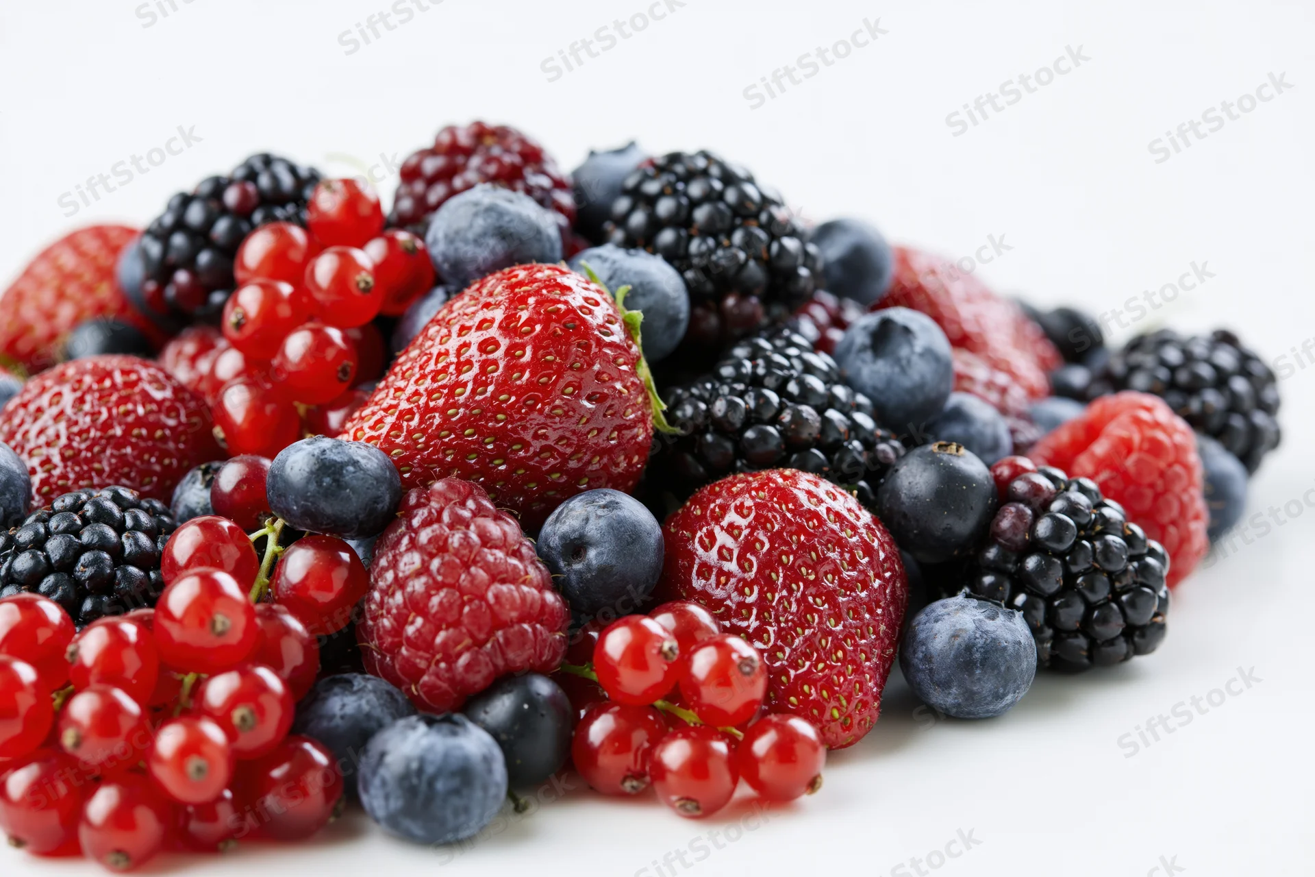 A pile of mixed fresh berries including strawberries, blueberries, blackberries and redcurrants on a white surface