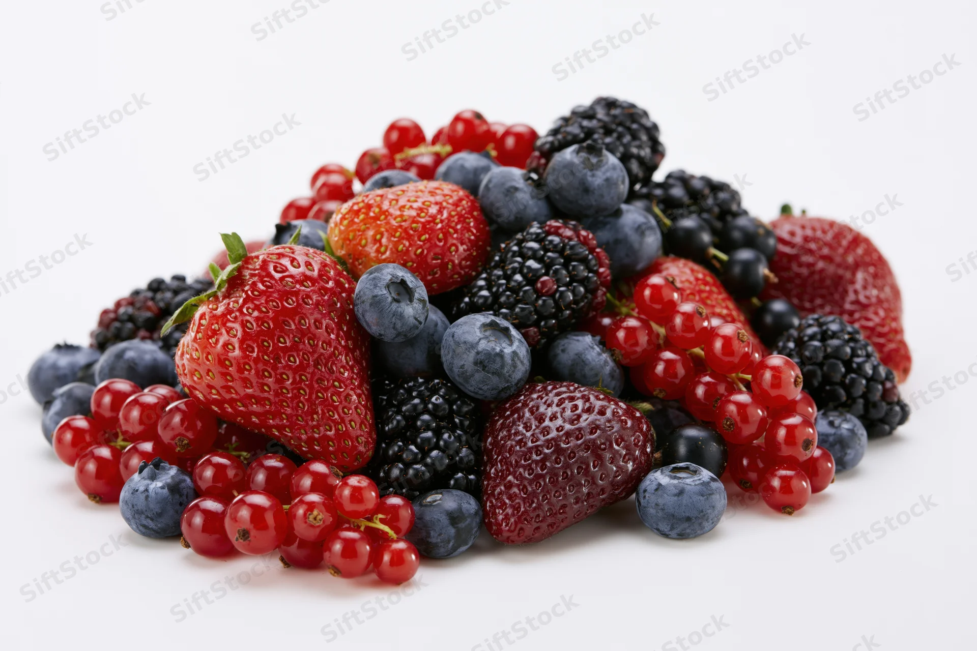 A pile of fresh strawberries blueberries blackberries and redcurrants on a white surface