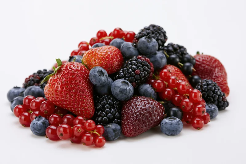 A pile of fresh strawberries blueberries blackberries and redcurrants on a white surface
