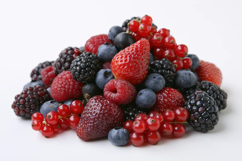 A pile of mixed fresh berries including strawberries, blueberries, blackberries and raspberries on a white background