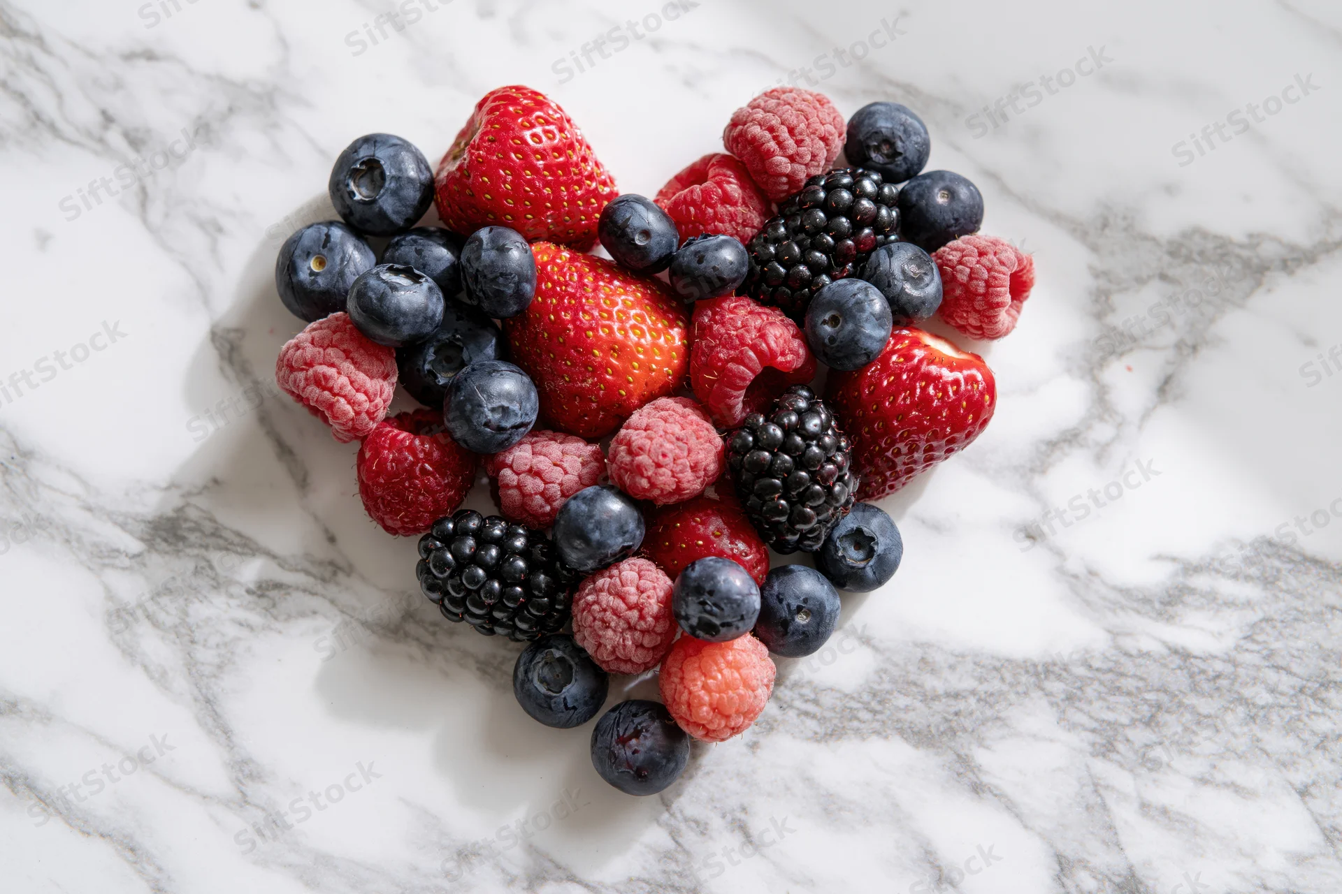 Mixed berries arranged in heart shape on marble surface