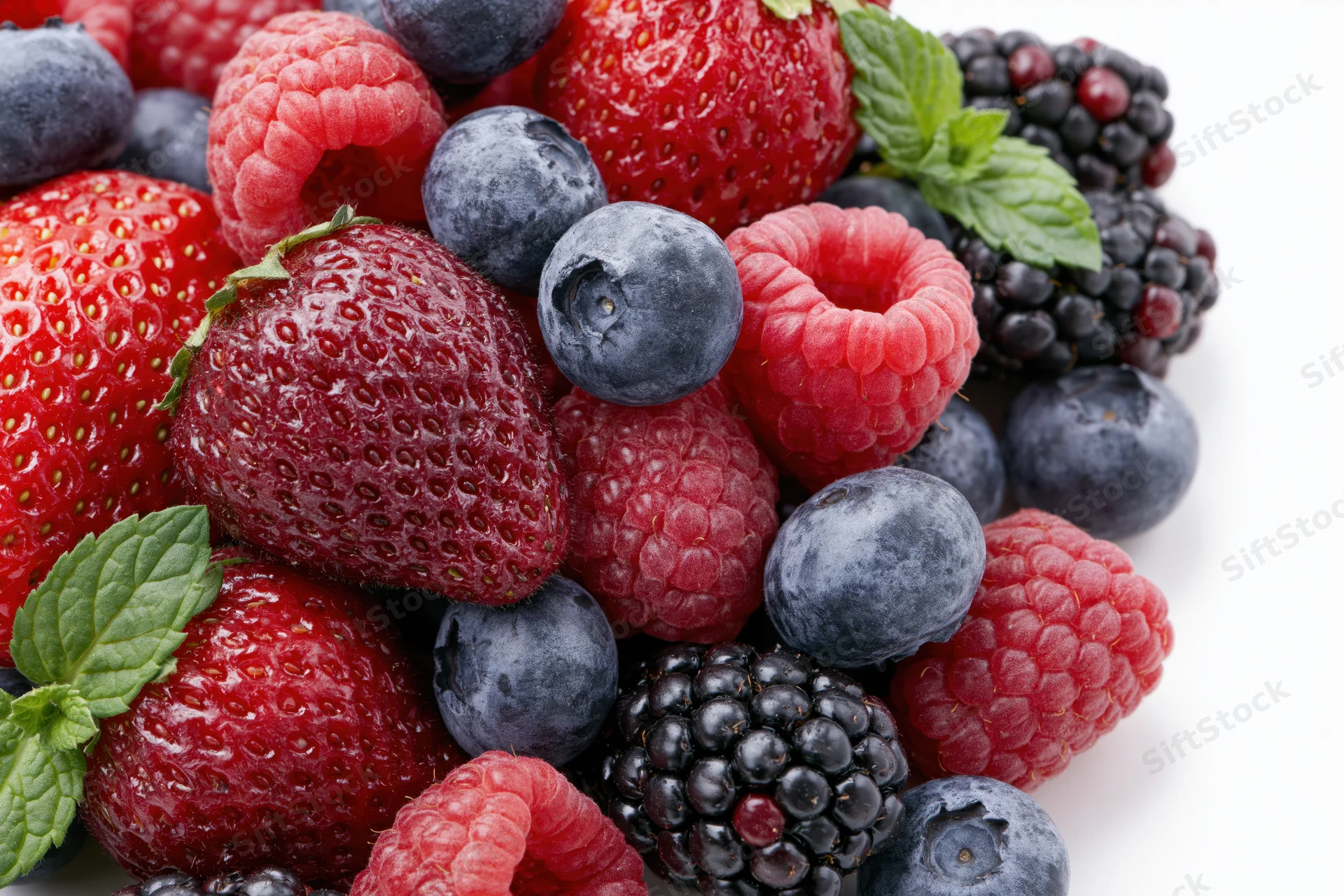 Mixed fresh berries including strawberries raspberries blackberries and blueberries with mint leaves on white background