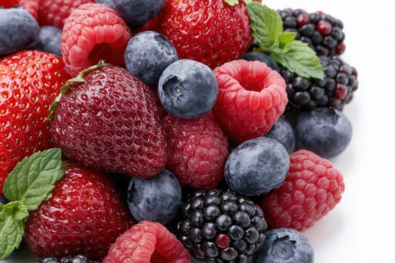 Mixed fresh berries including strawberries raspberries blackberries and blueberries with mint leaves on white background