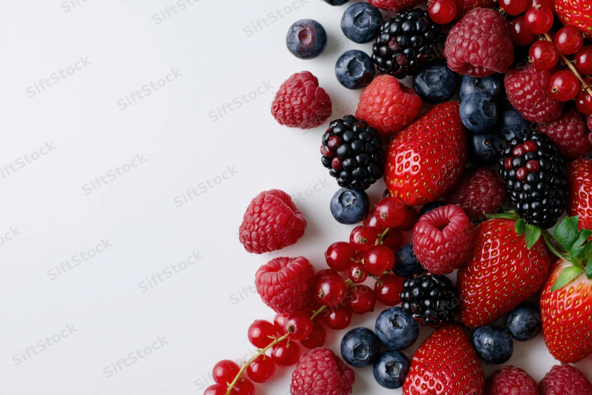 Mixed fresh berries arranged on white surface with copyspace on left