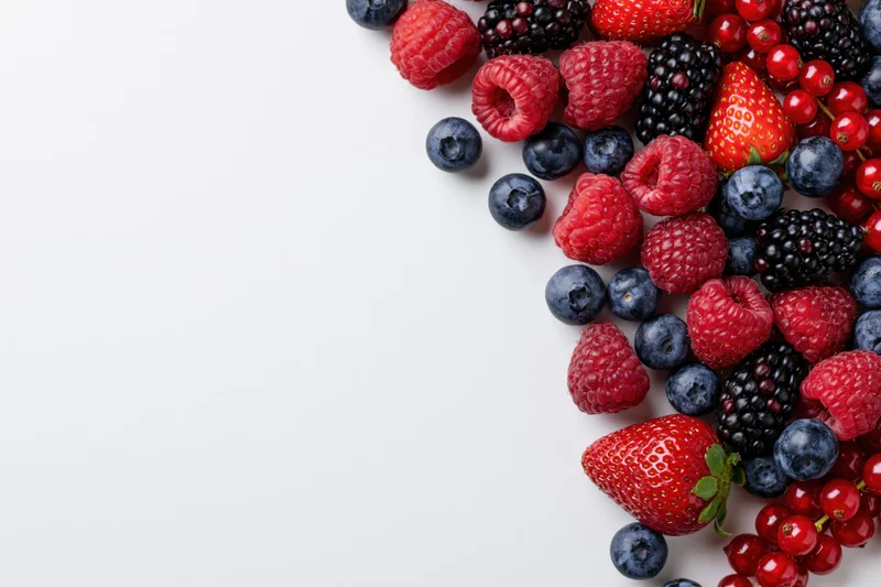 Mixed fresh berries arranged along the right edge on a white surface
