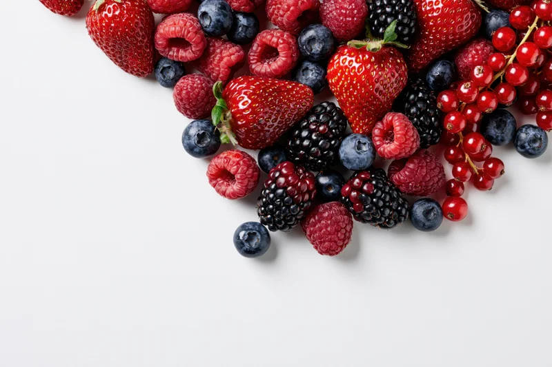 Mixed fresh berries arranged in a corner on a white surface with copyspace