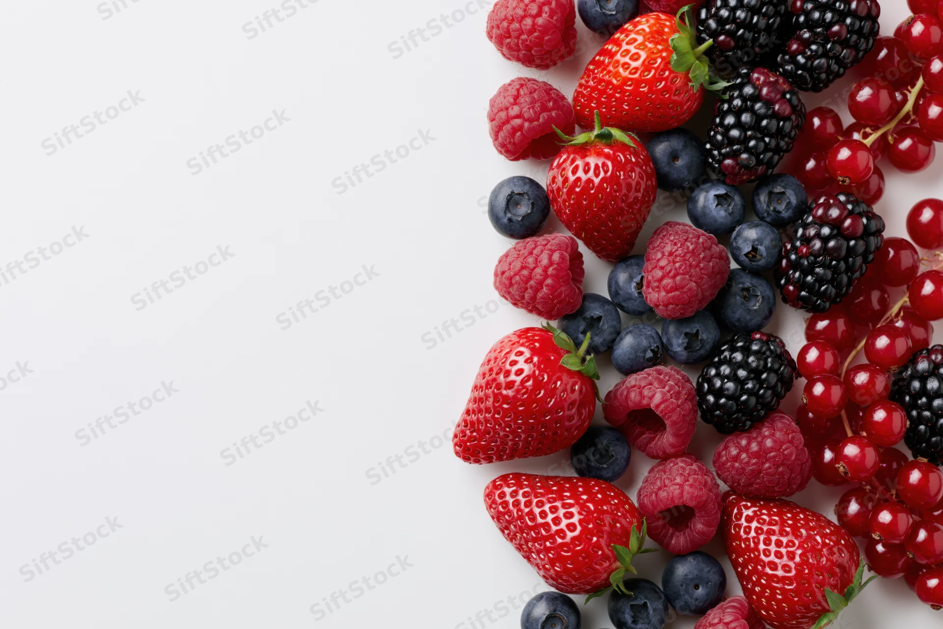 Mixed fresh berries arranged along the right side of a white surface with copyspace on the left