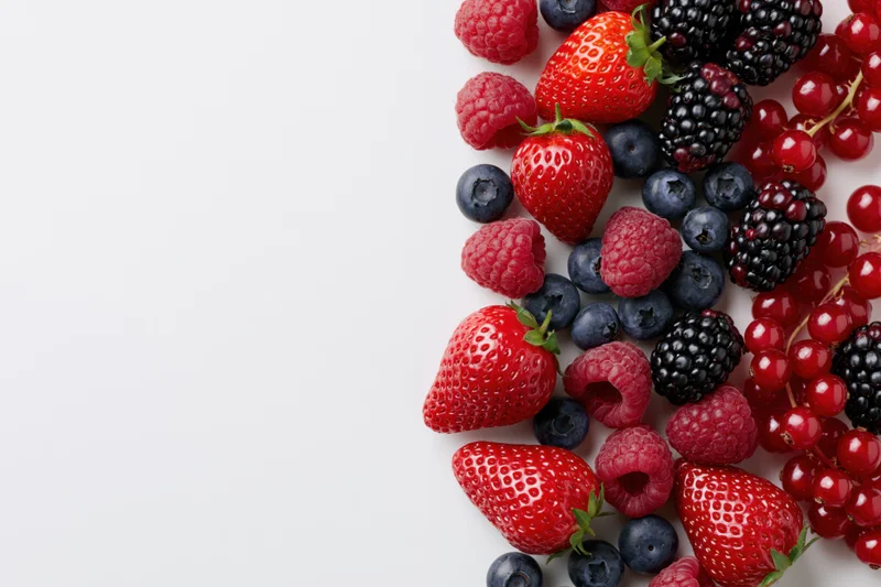 Mixed fresh berries arranged along the right side of a white surface with copyspace on the left