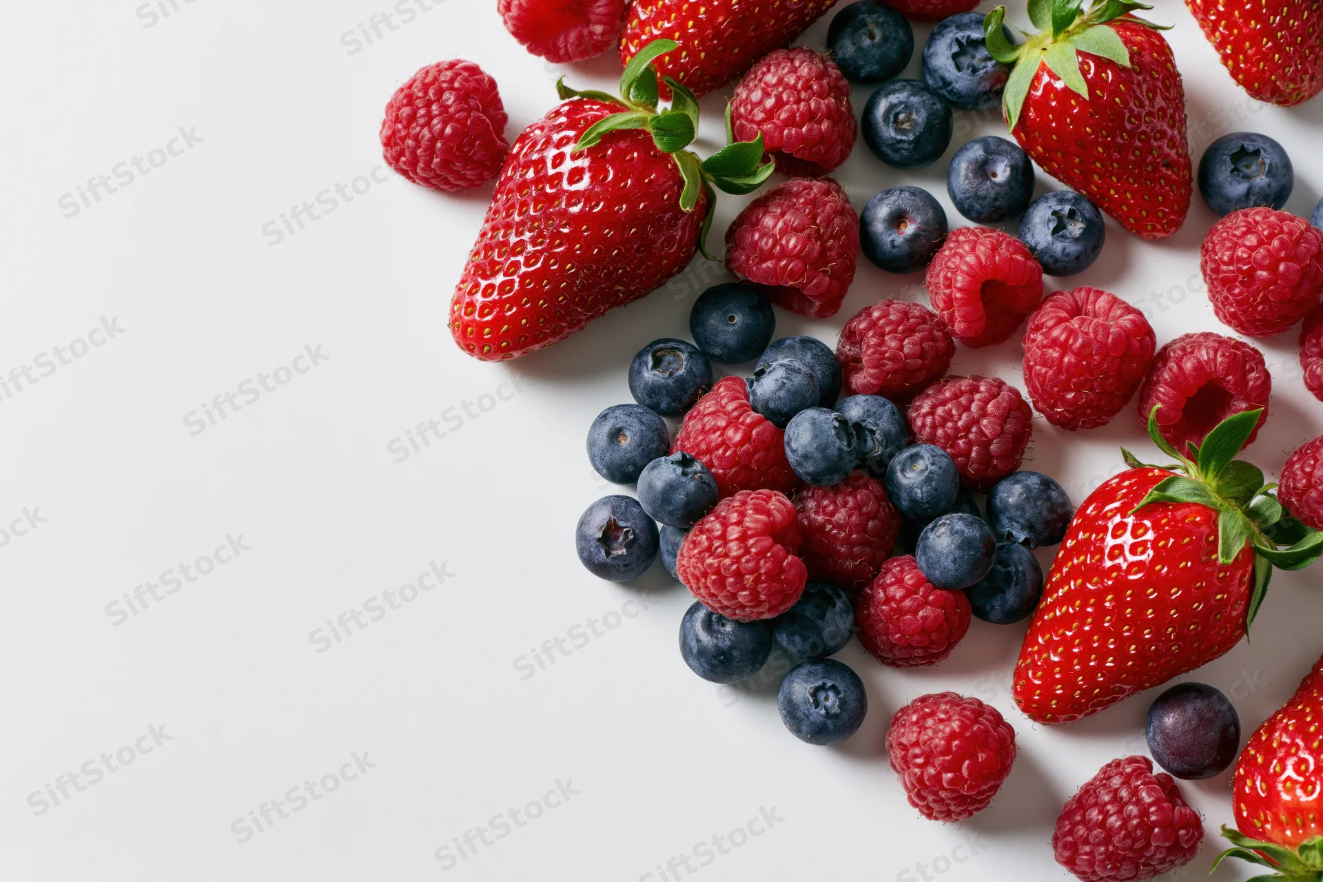 Mixed fresh strawberries raspberries and blueberries arranged on white surface with copyspace