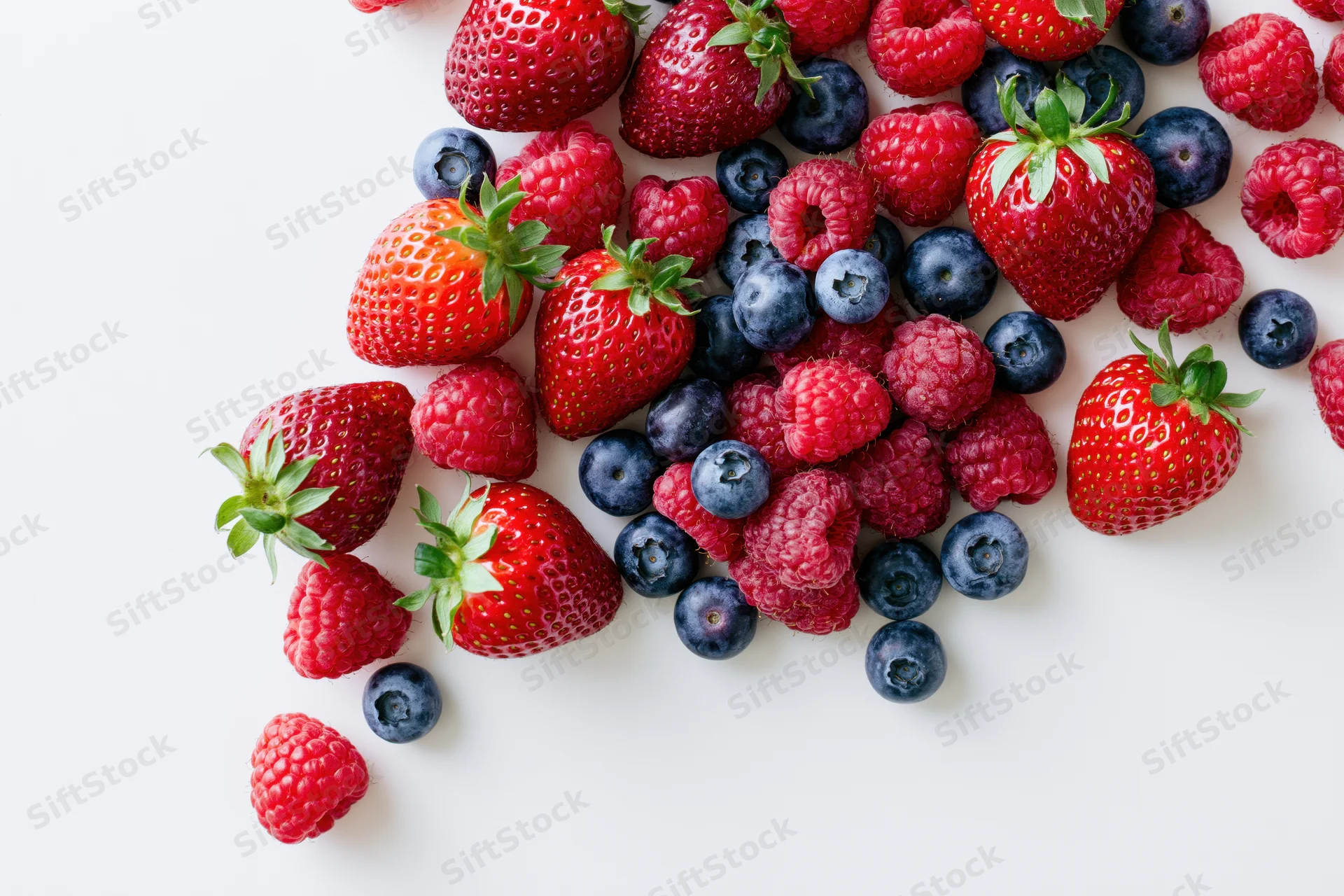 Mixed fresh strawberries raspberries and blueberries arranged on white surface