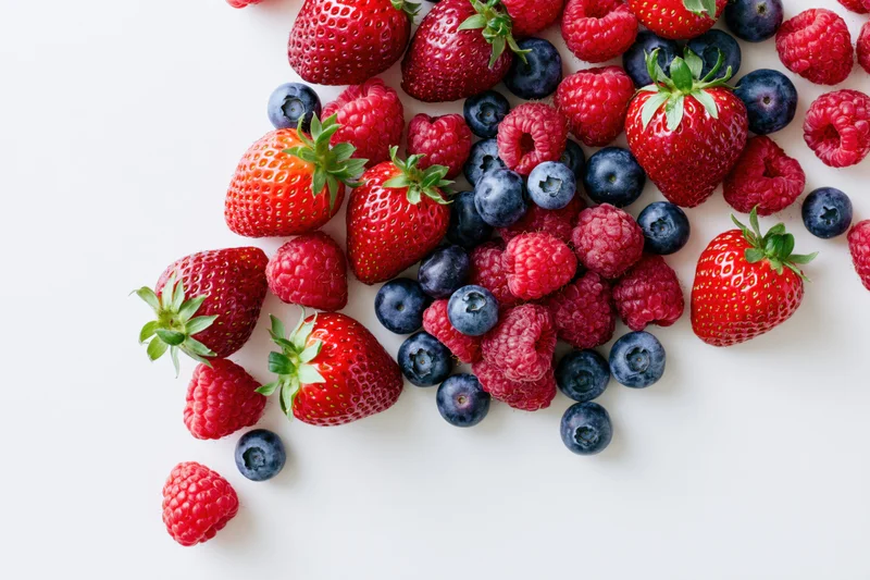 Mixed fresh strawberries raspberries and blueberries arranged on white surface