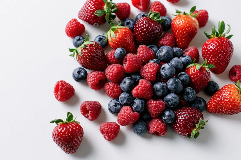 Mixed fresh strawberries raspberries and blueberries arranged on white surface