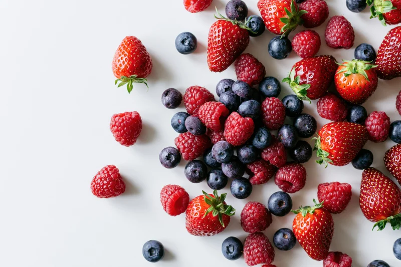 Mixed fresh strawberries raspberries and blueberries scattered on white surface with copyspace