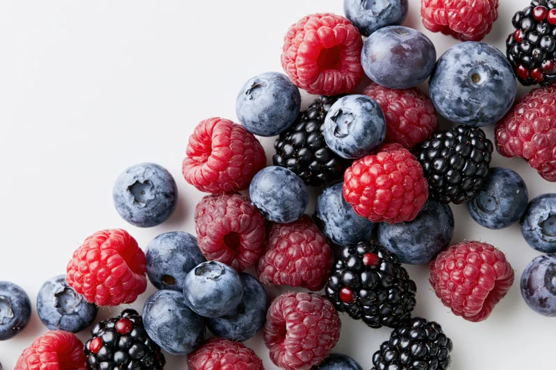 Mixed berries scattered on white surface with copyspace