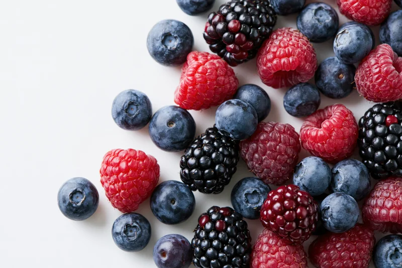 Mixed blueberries raspberries and blackberries scattered on white surface